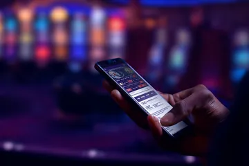 A man focused on his laptop with live stats in the background, highlighting the dedicated sports and gaming features of the AMJILI mobile app.